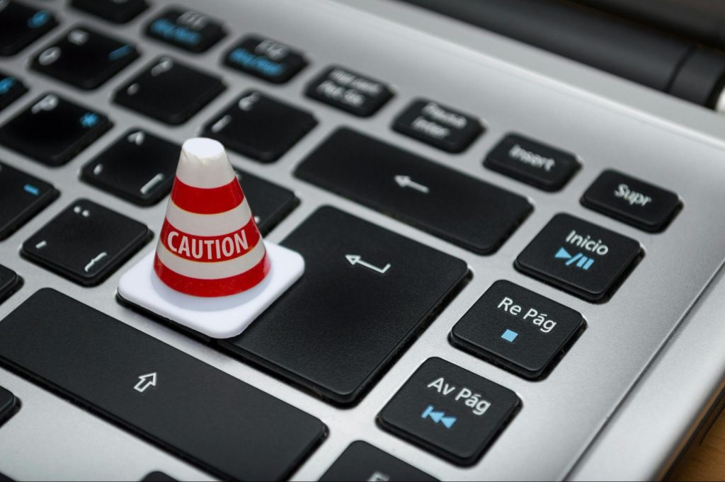 A photo of a computer keyboard with a miniature caution cone on top of the enter key.
