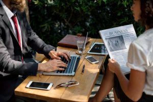 Two professionals having a meeting with a laptop and a newspaper in their hands.