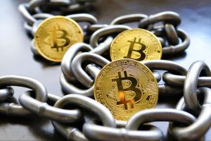 A loop of metal chain link with three gold bitcoin-engraved coins on top.